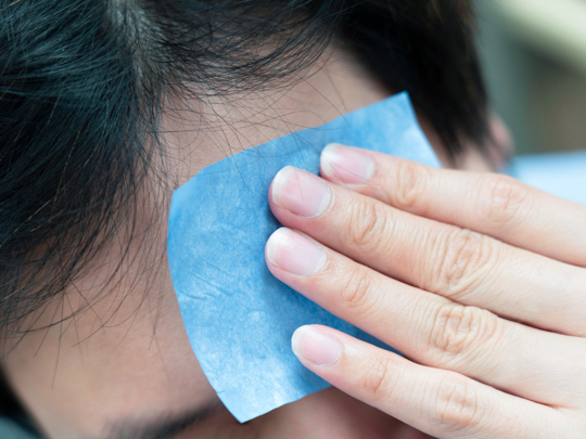 man wiping forehead with oil blotting paper